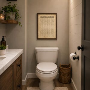 May include: A rectangular framed wall art piece featuring a word search puzzle titled 50 POTTY WORDS in black text on a beige background, displayed above a white toilet in a bathroom with a wooden vanity, a woven basket, and a toilet paper holder.