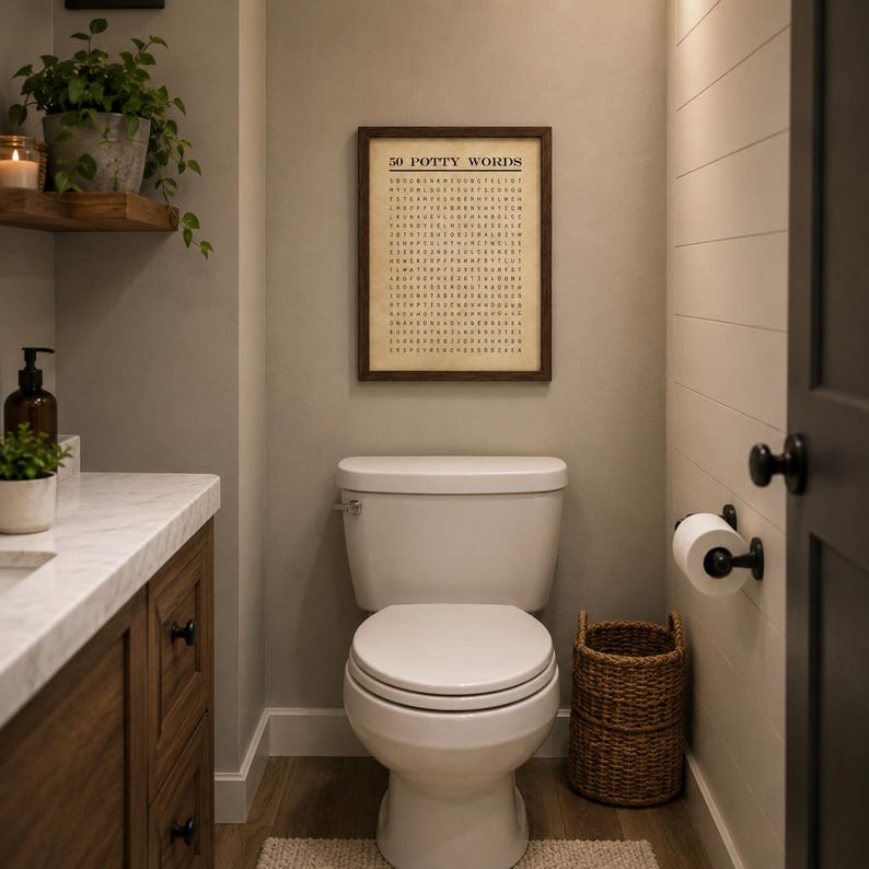 May include: A rectangular framed wall art piece featuring a word search puzzle titled 50 POTTY WORDS in black text on a beige background, displayed above a white toilet in a bathroom with a wooden vanity, a woven basket, and a toilet paper holder.