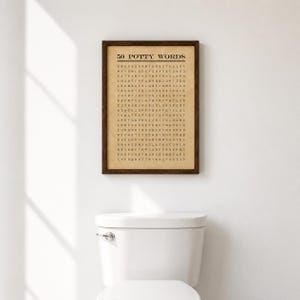 May include: A framed wall art print featuring a word search puzzle titled 50 POTTY WORDS in black text on a tan background. The grid contains various letters arranged in rows and columns. The frame is dark brown wood with a simple rectangular profile.