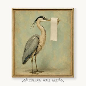 Pode incluir: Uma impressão de arte emoldurada apresentando uma garça cinzenta de perfil contra um fundo azul-claro suave. A ave segura um rolo de papel higiénico branco no seu bico longo e pontiagudo. A obra está contida numa moldura fina dourada.