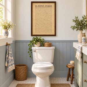 May include: A framed wall art print titled 50 POTTY WORDS featuring a word search puzzle in black text on a beige background. The print is displayed above a white toilet in a bathroom with blue wainscoting, a woven basket, and green plants.