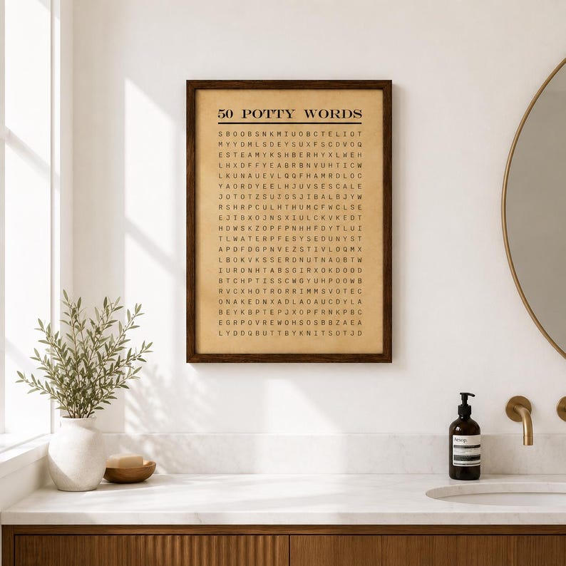 May include: A rectangular wall art print in a dark brown wooden frame featuring a word search puzzle titled 50 POTTY WORDS in black text on a tan background. The grid contains various letters arranged in rows and columns on a paper-like surface.