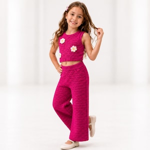 Puede incluir: Un conjunto de dos piezas de punto en color magenta brillante que consta de un top corto sin mangas y pantalones anchos. El top presenta tres aplicaciones de flores blancas en la parte delantera. La tela tiene una textura de punto acanalado.