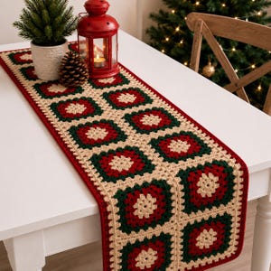 May include: A rectangular crochet table runner featuring a repeating granny square pattern in alternating colors of cream, forest green, and deep red. The runner is constructed from joined square motifs with a solid red border edge.