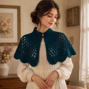 May include: A dark teal crochet capelet featuring an intricate openwork pattern, a scalloped hem, and a single gold-toned button closure at the neckline. The garment is worn over a long-sleeved, cream-colored dress with a simple, solid design.