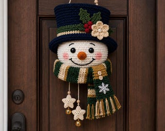 May include: A crocheted snowman wall hanging featuring a dark blue top hat adorned with green holly leaves, red berries, and a cream flower. The snowman has a white face, orange nose, and a striped green and cream scarf with two wooden buttons, a white snowflake, and two dangling cream stars with gold bells.