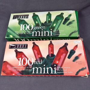 May include: Two rectangular boxes of 100 mini string lights. The top box is green with green bulbs, and the bottom box is red with red bulbs. Both boxes state 100 mini, lighted length 32', cord length 34', indoor/outdoor, and superbright bulbs.