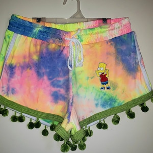 K&ouml;nnte beinhalten: Bunte Shorts im Batik-Look in Pink, Gelb, Blau und Gr&uuml;n. Die Shorts haben einen wei&szlig;en Kordelzug, wei&szlig;e Seitenstreifen und eine gr&uuml;ne Bord&uuml;re mit Bommeln. Ein gesticktes Bart Simpson-Motiv ist vorhanden.