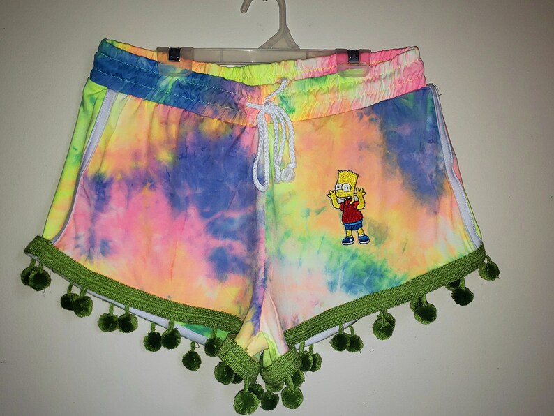 K&ouml;nnte beinhalten: Bunte Shorts im Batik-Look in Pink, Gelb, Blau und Gr&uuml;n. Die Shorts haben einen wei&szlig;en Kordelzug, wei&szlig;e Seitenstreifen und eine gr&uuml;ne Bord&uuml;re mit Bommeln. Ein gesticktes Bart Simpson-Motiv ist vorhanden.