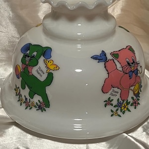 Op de afbeelding: Een witte melkglazen lampenkap met een gegolfde bovenrand. De kap is voorzien van kleurrijke cartoonillustraties van een groene puppy met het label Puppy Patch en een roze kitten met het label Pussy Fluff, omringd door kleine bloemen en vogels.