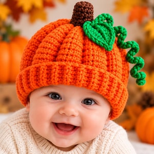 Puede incluir: Un gorro de ganchillo naranja brillante con forma de calabaza, que presenta un borde acanalado, un tallo marrón oscuro en la parte superior y una hoja verde tejida con un zarcillo rizado en el lateral. Tiene relieves verticales de calabaza.