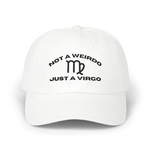 May include: A white baseball cap featuring black text that reads NOT A WEIRDO in an arc above a black Virgo zodiac symbol, with the text JUST A VIRGO printed in a straight line below the symbol. The cap has a curved brim and a structured crown.