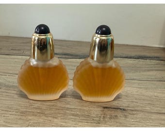 May include: Two identical perfume bottles shaped like seashells with frosted glass bodies containing amber-colored liquid. Each bottle features a metallic gold neck and a small, rounded dark blue cap, creating a uniform appearance for the pair.