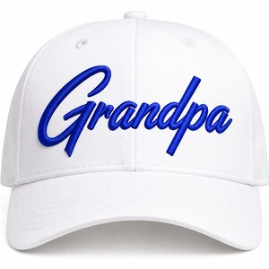 May include: A white baseball cap featuring the word "Grandpa" embroidered in a bold, blue cursive script across the front panels. The cap has a structured crown, a curved brim, and stitched eyelets for ventilation on the top panels.