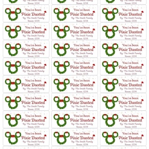 May include: A sheet of rectangular stickers featuring a green wreath shaped like a mouse head with a red bow. The text reads: You've been Pixie Dusted, By: The Smith Family, Room: 1234. The background has a faint pattern of small snowflakes.