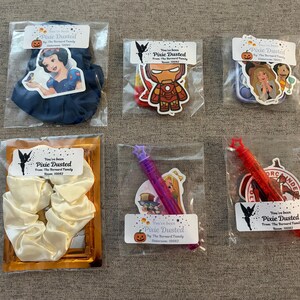 May include: Six individual gift bags containing various items including a dark blue scrunchie with a Snow White sticker, an Iron Man pop-it toy, a multi-character sticker set, a white scrunchie, a purple bubble wand, and a red bubble wand with a Spider-Man sticker.