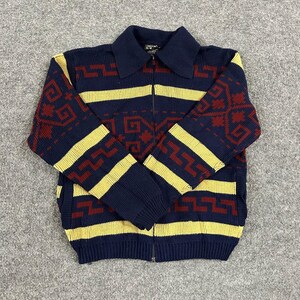 May include: A navy blue zip-up knit sweater featuring a prominent collar and a repeating geometric pattern in dark red and yellow. The long-sleeved garment includes horizontal yellow stripes and ribbed cuffs, showcasing a textured knit construction.