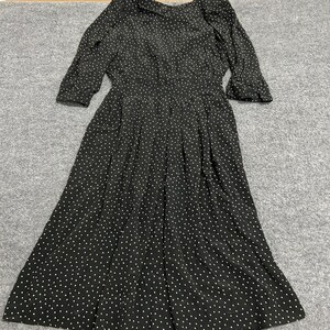 May include: A black midi dress featuring a repeating pattern of small white triangles. The garment has three-quarter length sleeves, a round neckline, a fitted waistline, and a pleated skirt that falls below the knees in a flared silhouette.