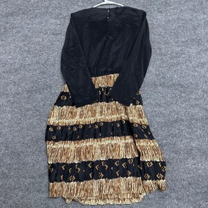 May include: A long-sleeved dress featuring a solid black bodice and a pleated skirt. The skirt displays horizontal bands of metallic gold fringe alternating with black fabric sections decorated with a repeating geometric diamond pattern.