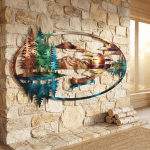May include: An oval metal wall art piece featuring a landscape scene with copper and teal pine trees, mountains, a sun, and a canoe. The design includes a reflection of the trees in the water below, all enclosed within a thin, dark metal frame.