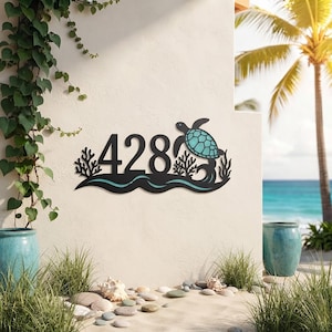 May include: A black metal house number sign displaying the digits 428, featuring a teal sea turtle, coral, and wave motifs. The design is a flat, cut-out style with a horizontal orientation, showcasing a marine theme with aquatic elements.