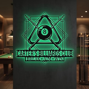 May include: A wall-mounted neon sign featuring a glowing green light. The design includes a black 8-ball inside a triangle, crossed pool cues, and the text CARTER'S BILLIARDS CLUB and BREAK AIM WIN in a bold, sans-serif font on a dark surface.