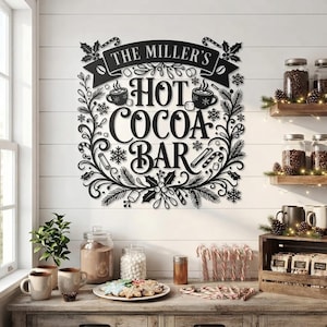 Könnte beinhalten: Ein schwarzes Metall-Wandschild mit der Aufschrift THE MILLER'S HOT COCOA BAR, umgeben von dekorativen Illustrationen von Tassen, Zuckerstangen, Marshmallows, Tannenzweigen und Stechpalmenblättern, montiert an einer weißen Holzwand.