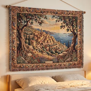 Puede incluir: Un tapiz de pared tejido rectangular que muestra una escena de un pueblo costero mediterráneo con edificios de piedra, cipreses y vistas al mar. El borde presenta motivos frutales y el texto MONTE SOLARI es visible en la parte inferior central.