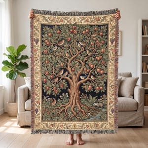 May include: A woven throw blanket featuring a detailed tapestry design of a large tree filled with red apples and various birds. The scene includes a rabbit and a badger at the base, surrounded by foliage, all framed by a decorative floral border.