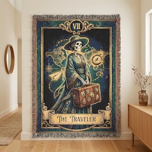 Peut inclure: Un plaid tissé représentant une carte de tarot intitulée The Traveler. L'image montre un squelette portant un chapeau et une robe, tenant une valise devant une carte du monde avec une boussole et un avion en papier. La bordure est ornée.