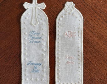 Pode incluir: Dois marcadores de página de tecido off-white com bordas e detalhes bordados. O da esquerda tem uma cruz e o texto azul "Mary Renard Burns" e "February 28 2025". O da direita tem um motivo floral e o texto rosa "ABC" e "June 2025".