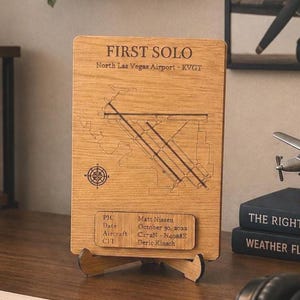 May include: A rectangular wooden plaque featuring an engraved map of North Las Vegas Airport, the text FIRST SOLO, and a compass rose. A smaller wooden plate displays flight details including the date October 30, 2022, and aircraft C172N.