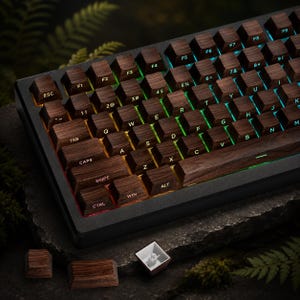 May include: A mechanical keyboard featuring dark brown wood grain keycaps with white lettering and integrated RGB backlighting. The keyboard has a black frame, and two loose wood grain keycaps are placed in front, one showing the white plastic underside.