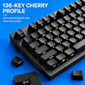 Könnte beinhalten: Eine schwarze mechanische Tastatur mit 136 Cherry-Profil-Tastenkappen, die seitlich aufgedruckte Beschriftungen und eine saubere Oberseite aufweisen. Der Text 136-KEY CHERRY PROFILE und Side-printed legends only. Clean top surface. ist zu sehen.
