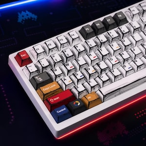 May include: A mechanical keyboard featuring white keycaps with black comic-style line art and various colored accent keys including red, yellow, blue, and black. The keys display standard QWERTY lettering and function labels with small colored dashes.