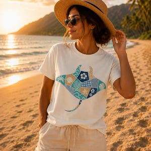 Könnte beinhalten: Ein weißes Kurzarm-T-Shirt mit einer großen Mantarochen-Grafik, die aus verschiedenen blauen, beigen und weißen Patchwork-Mustern besteht, darunter Blumen-, Vichy-Karo- und Wellendesigns. Das T-Shirt hat einen Rundhalsausschnitt und eine lockere Passform.