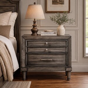 May include: A gray wooden nightstand with three drawers featuring two small round silver knobs on the top two drawers and a long rectangular silver handle on the bottom drawer, supported by four sturdy legs with a distressed finish.