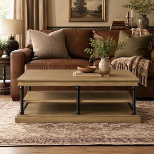 May include: A rectangular coffee table with a light brown wooden top and a matching lower shelf. The table features four black metal legs with a rounded, spindle-like design. The surface holds a small wooden bowl and a stack of two books.