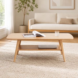 May include: A light-toned wooden coffee table with rounded corners and four tapered legs. The table features a lower shelf holding a closed laptop, while the top surface displays an open book and a clear glass tumbler filled with water.