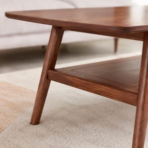 May include: A dark brown wooden coffee table featuring a smooth rectangular top with rounded corners, angled legs, and a lower shelf. The wood grain is visible across the surface, showcasing a natural finish on the frame and the lower shelf.