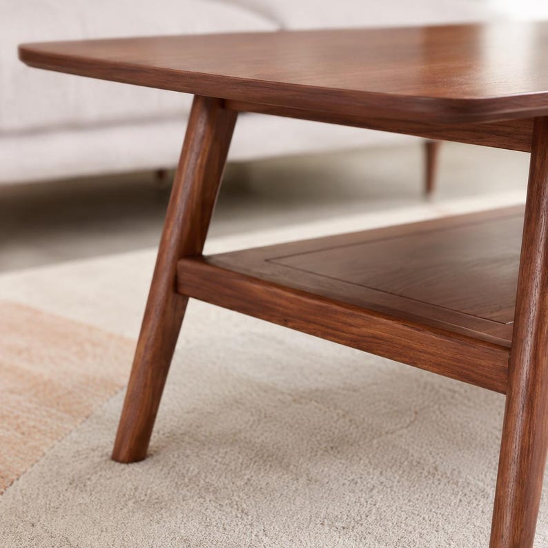 May include: A dark brown wooden coffee table featuring a smooth rectangular top with rounded corners, angled legs, and a lower shelf. The wood grain is visible across the surface, showcasing a natural finish on the frame and the lower shelf.
