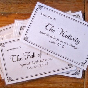 May include: A set of white cards with black text and borders. The cards feature the titles "The Nativity" and "The Fall of" with corresponding scripture references and symbols. The cards are labeled with the dates December 24 and December 3.