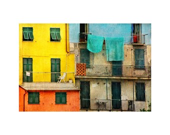 Può includere: Un edificio colorato con più balconi e finestre. L'edificio è dipinto in tonalità di giallo, arancione e blu. Ci sono persiane verdi alle finestre e una sedia bianca su uno dei balconi.
