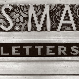 May include: A vintage silver mailbox with the word "LETTERS" in raised lettering on a black background and the word "SMA" in raised lettering on a decorative background.