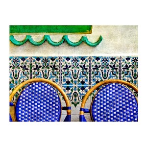 May include: Two blue and white wicker chairs with wooden frames sit in front of a wall with green and blue patterned tiles.