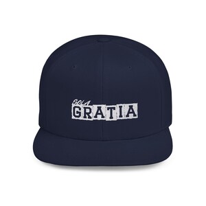 May include: A navy blue baseball cap featuring the embroidered text "SOLA GRATIA" in white. The word "SOLA" is positioned above the word "GRATIA," which is displayed in a bold, block-letter font with a white rectangular background behind each letter.