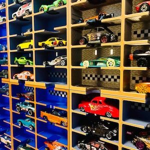 May include: A wall-mounted display rack with multiple rectangular compartments holding various miniature toy cars. The rack features a blue and gold color scheme with a black and white checkered pattern along the back edges of the shelves.