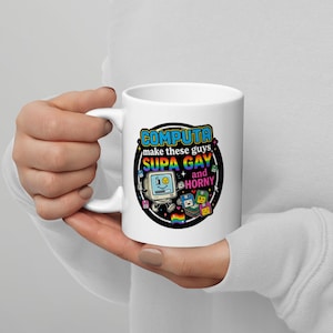 Puede incluir: Una taza de cerámica blanca con un diseño gráfico que muestra un ordenador retro, disquetes de colores y el texto "COMPUTA make these guys SUPA GAY and HORNY" rodeado por un borde circular negro con pequeños corazones y estrellas.