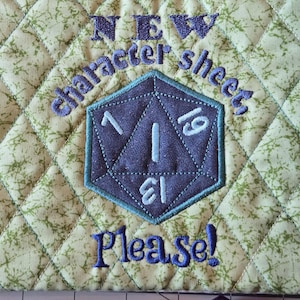 May include: A quilted light green fabric pouch featuring a dark blue embroidered twenty-sided die in the center. The text "NEW character sheet" is embroidered in blue above the die, and "Please!" is embroidered in blue below the die.