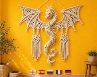 May include: A large, off-white macrame wall hanging shaped like a dragon with intricate knotted patterns, expansive wings, and a long, curved tail. The piece is suspended by a cord and features decorative fringe hanging from the lower wing sections.